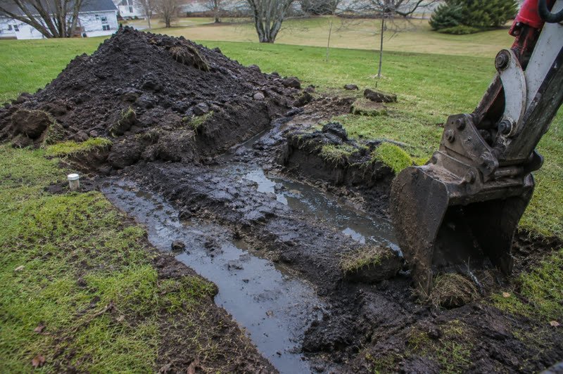 Open septic tank access riser beside an excavated trench on a rural property